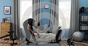 Handsome Young Man in a Black T-Shirt and black gym suit doing stretching at home. Handsome Guy doing warm up in Living Room at