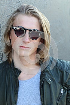 Handsome young man with blond long hair and sunglasses isolated on grey background. Fashion studio shot