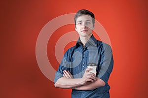 Handsome young man in blue shirt with rolled sleeves with crossed arms holding coffee in paper cup and looking at camera