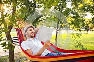Handsome young man with book resting in hammock outdoors