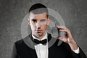 Handsome young man with bottle of perfume on grey background