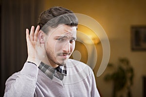 Handsome young man can't hear, putting hand around his ear