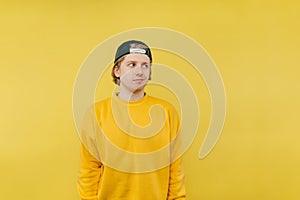 Handsome young man in a cap and yellow sweatshirt stands on a colored background and looks away