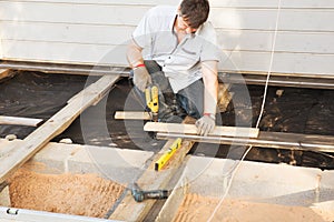 Handsome young man carpenter installing a wood floor outdoor terrace in new house construction site