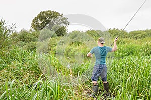 Handsome young man casts a spinning rod on the river bank