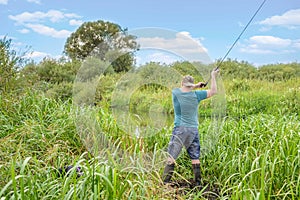 Handsome young man casts a spinning rod on the river bank