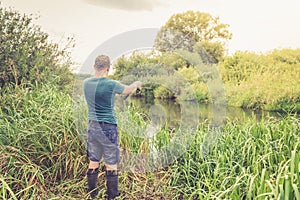 Handsome young man casts a spinning rod on the river bank