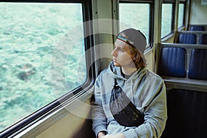 Handsome young man in casual clothes rides in a train and looks out the window