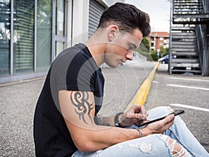 Young man using tablet PC sitting on street curb