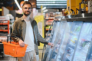 Handsome young man check the fridges for frozen food in the supermarket.