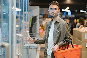 Handsome young man check the fridges for frozen food in the supermarket.