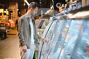 Handsome young man check the fridges for frozen food in the supermarket.