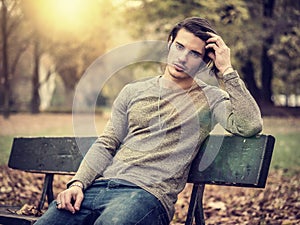 Handsome young man in city park, sitting on a bench