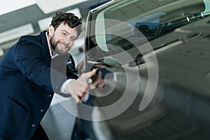 Handsome young man in classic blue suit is smiling while examining car in a motor show