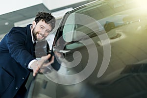 Handsome young man in classic blue suit is smiling while examining car in a motor show