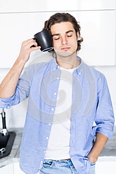 Handsome young man with coffee cup near head, suffer from pain, in the morning at kitchen