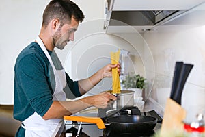 Handsome young man cooking pasta in the kitchen at home