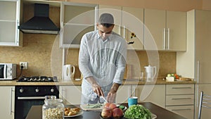 Handsome young man cooking vegetarian breakfast cutting vegetables for salad in kitchen at home