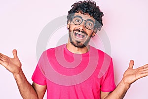 Handsome young man with curly hair and bear wearing casual clothes and glasses celebrating victory with happy smile and winner