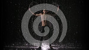 Handsome young man dancing modern ballet splitting raindrops. Male dancer with a naked torso moves plastically on a