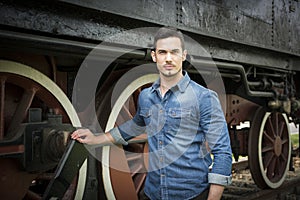 Handsome young man in denim shirt in front of old train