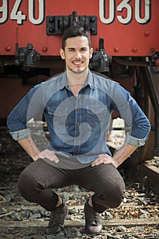 Handsome young man in denim shirt in front of old train