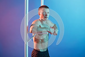 Handsome young man doing exercise on horizontal bar, guy posing topless, keeps fit, posing isolated over neon background, male