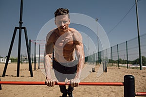 Handsome young man doing street workout on the beach in a bright summer day