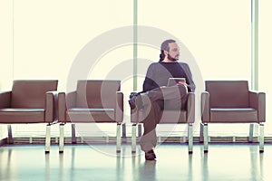 Handsome young man with dreadlocks using his digital tablet pc at an airport lounge, modern waiting room, with backlight