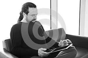 Handsome young man with dreadlocks using his digital tablet pc at an airport lounge, modern waiting room, with backlight