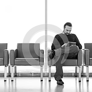 Handsome young man with dreadlocks using his digital tablet pc at an airport lounge, modern waiting room, with backlight