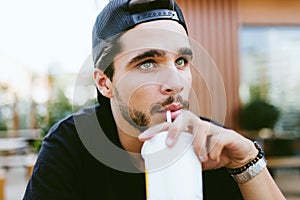 Handsome young man drinking refreshment at outdoor bar.