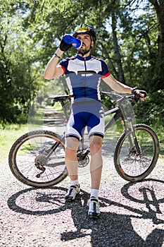 Handsome young man drinking water after cycling in the mountain.