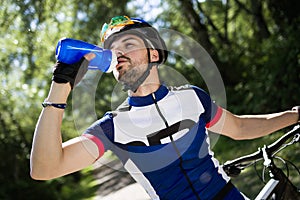 Handsome young man drinking water after cycling in the mountain.