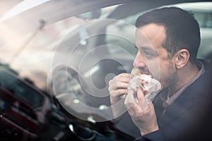 Handsome young man eating a hurried lunch in his car