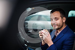 Handsome young man eating a hurried lunch in his car