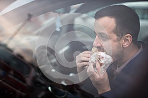 Handsome young man eating a hurried lunch in his car