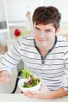 Handsome young man eating a salad in the kitchen