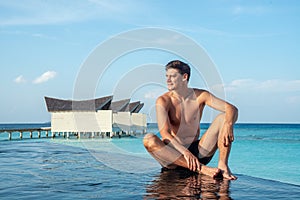 Handsome young man at the edge of infinity swimming pool at the tropical island luxury resort