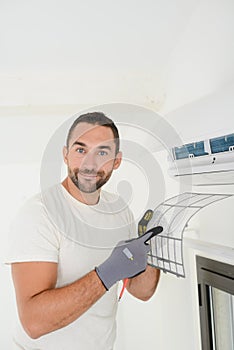 Handsome young man electrician cleaning air filter on an indoor unit of an air conditioning in a client house