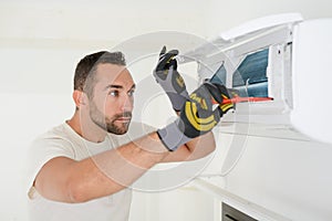 Handsome young man electrician cleaning air filter on an indoor unit of an air conditioning in a client house