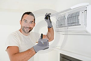 Handsome young man electrician cleaning air filter on an indoor unit of an air conditioning in a client house