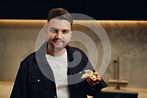 Handsome young man enjoying pizza in his kitchen. Unbelievably enjoys the taste