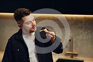 Handsome young man enjoying pizza in his kitchen. Unbelievably enjoys the taste