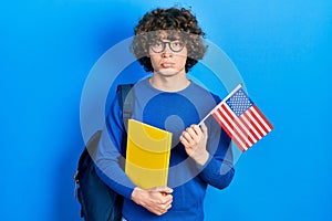 Handsome young man exchange student holding usa flag depressed and worry for distress, crying angry and afraid