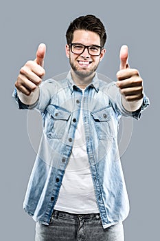 Handsome young man expressing happiness with thumb up over gray background.