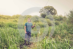 Handsome young man with a fishing rod on the river bank