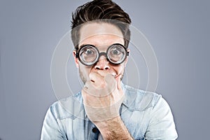 Handsome young man with funny glasses joking and making funny face over gray background.