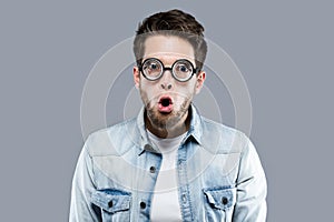 Handsome young man with funny glasses joking and making funny face over gray background.