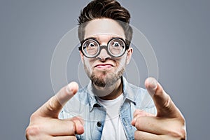 Handsome young man with funny glasses joking and making funny face over gray background.